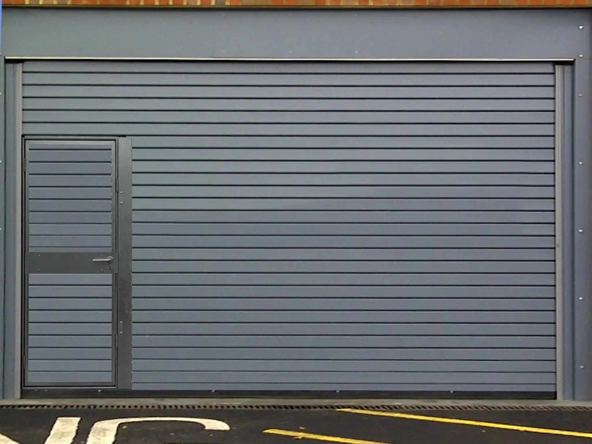 Manually operated roller shutter door with wicket door in grey