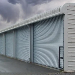 Steel building fitted with four manually operated roller shutter doors with wicket door access to the first door